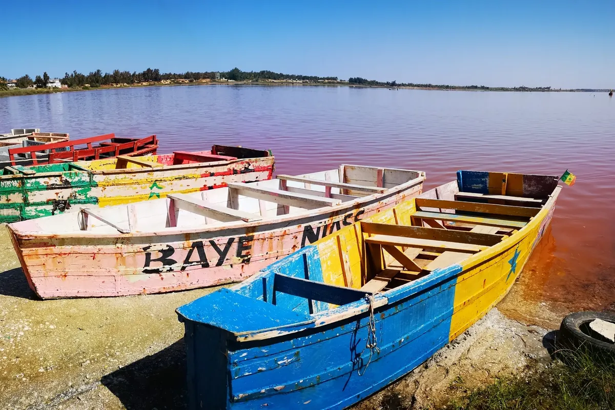 Des barques colorées sur la rive du lac Rose, à l’eau teintée de rose