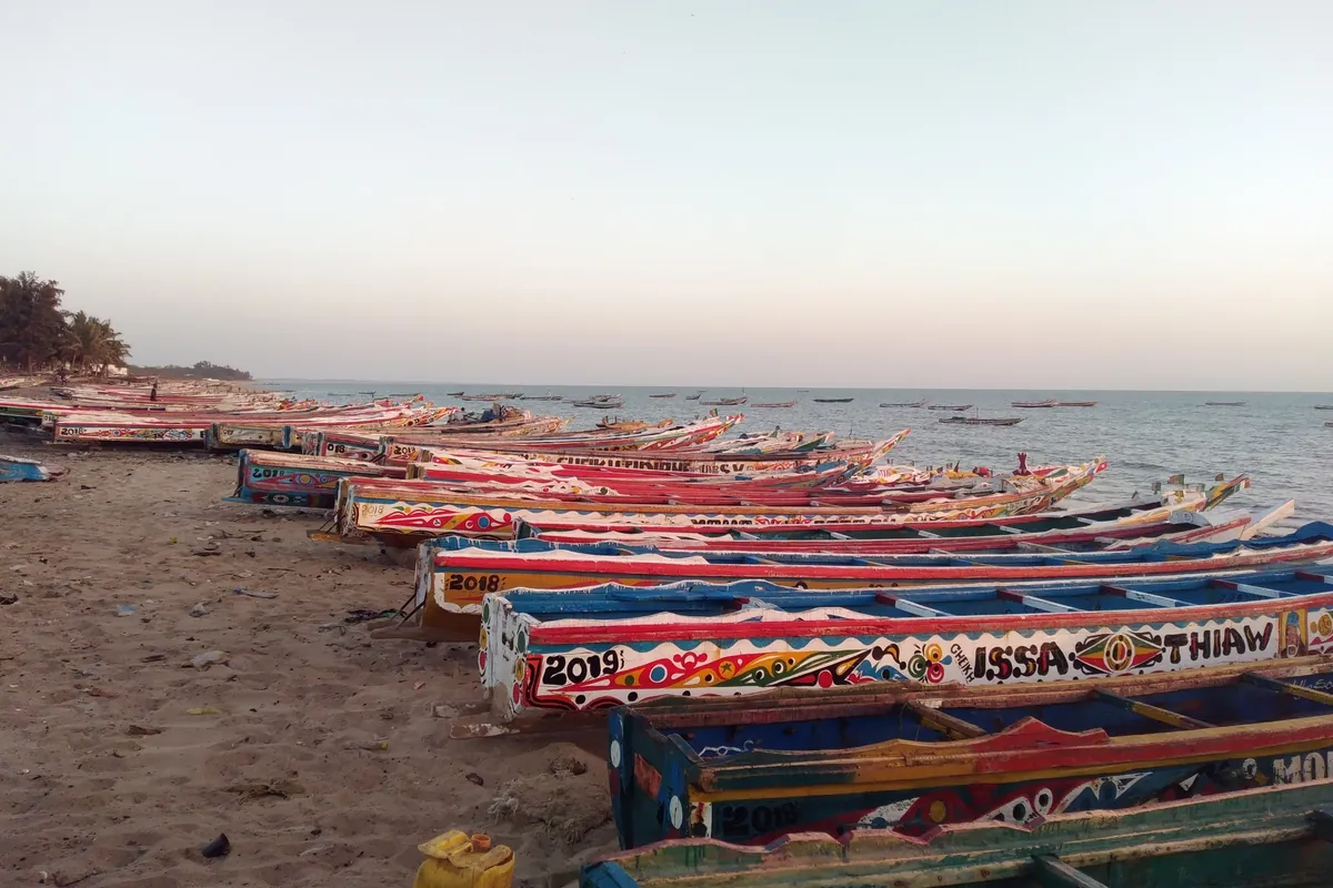 Une longue file de pirogues peintes alignées sur la plage de Mbour au crépuscule
