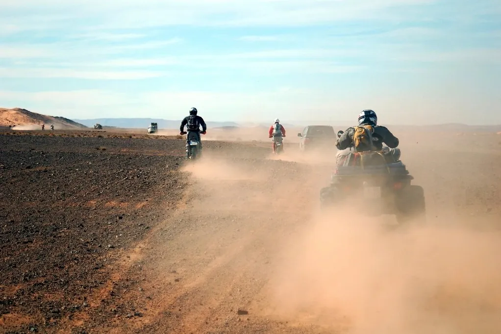 Des quads soulèvent un nuage de poussière ocre sur une piste